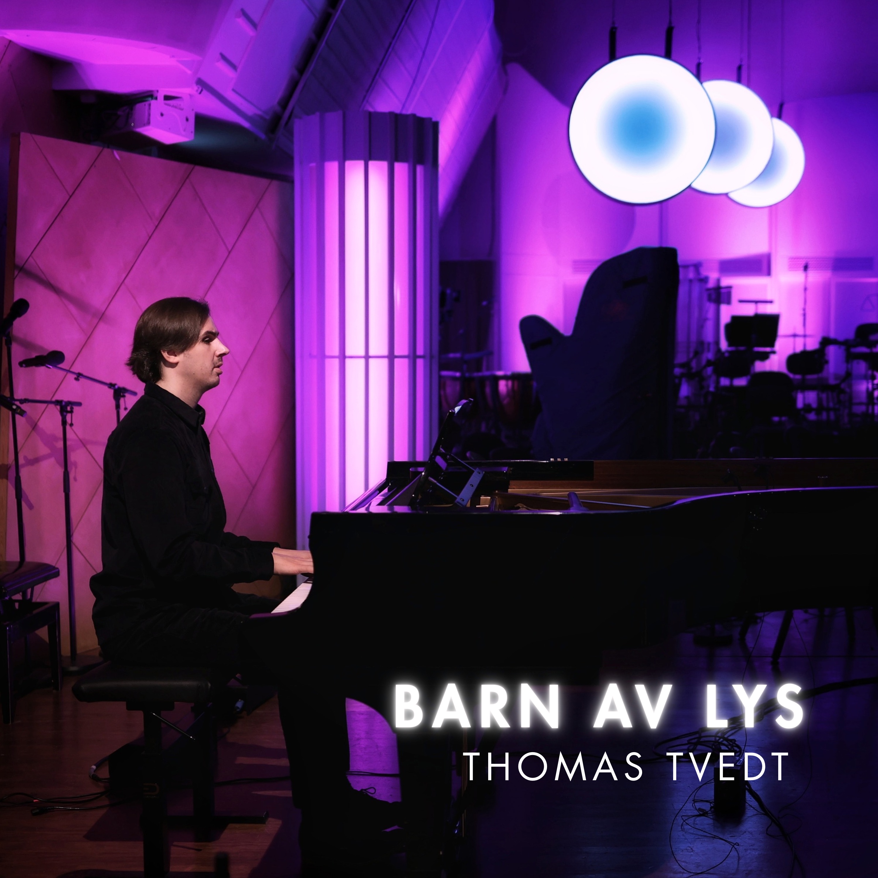 Cover for «Barn av lys»: Thomas ved flygelet i et studio badet i lilla og blått lys, med tre runde lamper på veggen.